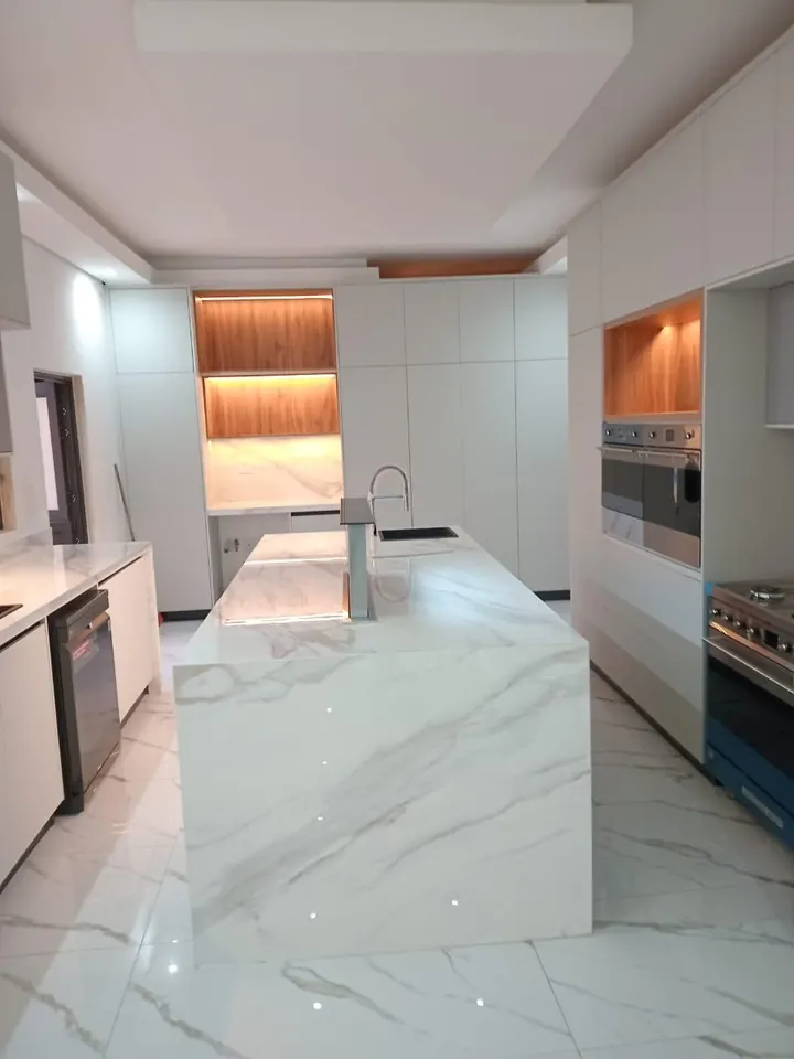 White kitchen with marble-look island, tall units and built-in ovens